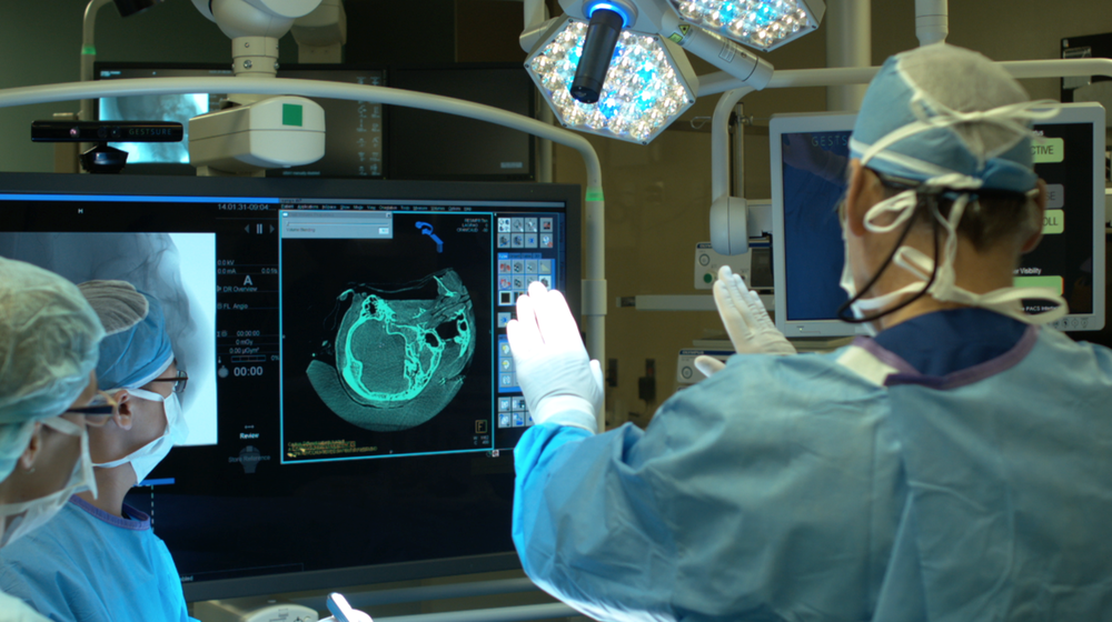 Surgeons in an operating room using GestSure to review a CT scan on the OR monitor.